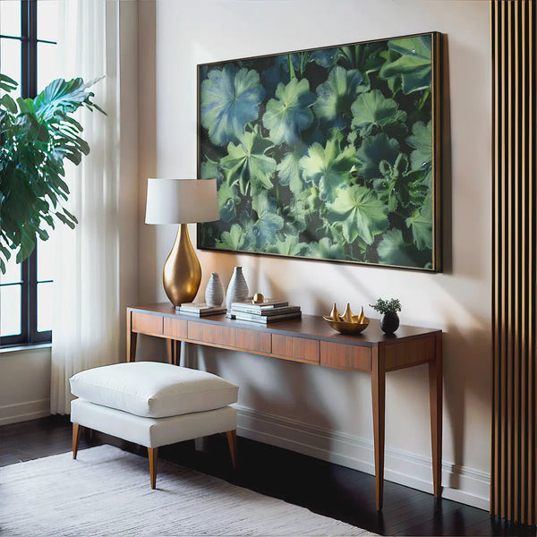 Großformatiges Wandbild mit detailreicher Blatt-Naturfotografie in Grün, präsentiert über einer eleganten Holzkonsole in einem stilvoll eingerichteten Wohnraum mit Designlampe und hellen Textilien – beruhigende, ästhetische Naturkunst für moderne Interiors.